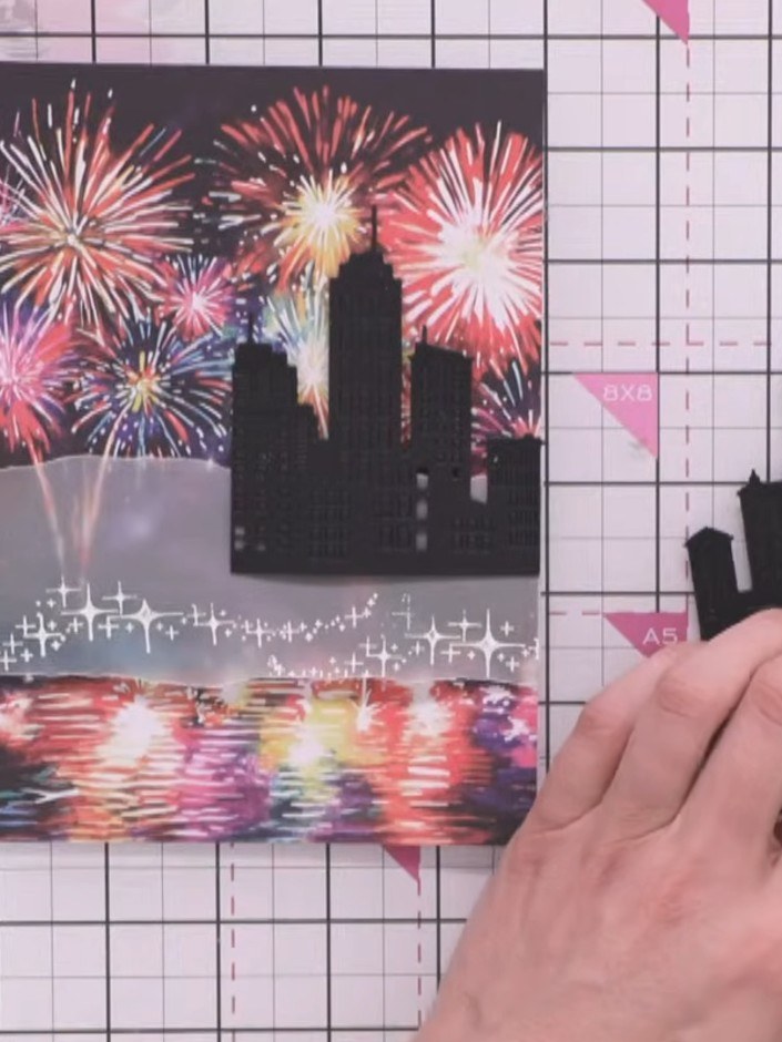 Step 9: Position a smaller black die-cut cityscape piece behind the vellum overlay to add depth. Use a white or gold g