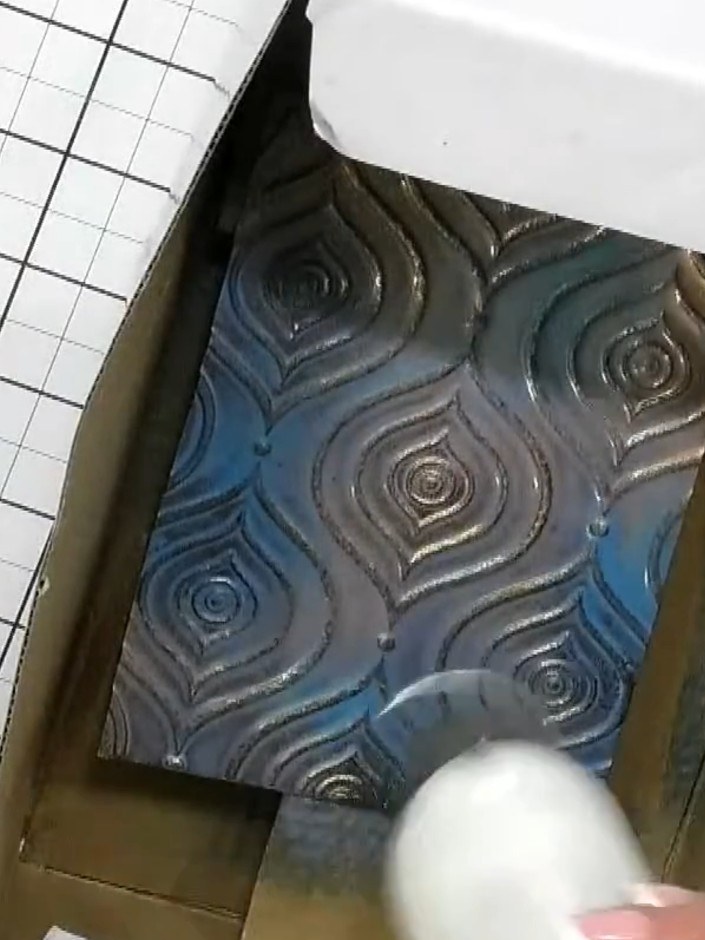 Step 4: Spray the embossed card with blue acrylic spray, layering it over the metallic colours to create a mixed effec