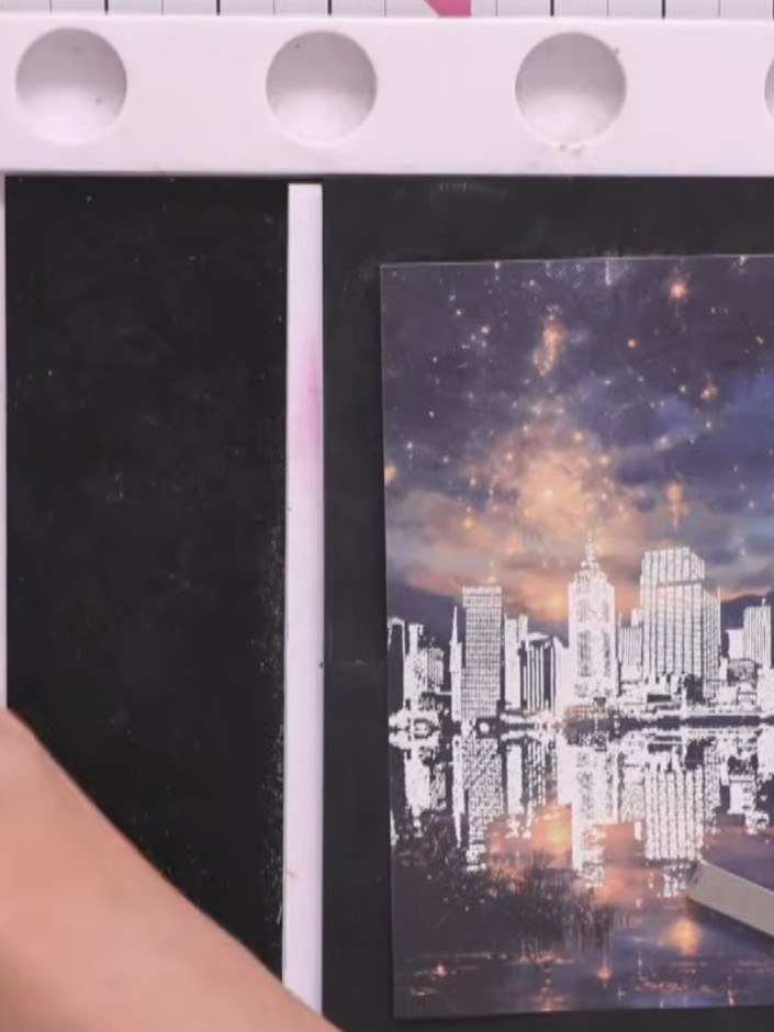 Step 4: Stamp the cityscape reflection and fireworks design onto your chosen paper, positioning the fireworks in the u