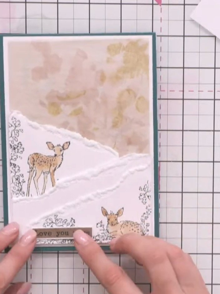 Step 9: Add a sentiment banner reading 'love you more' near the base of the card, positioning it centrally below the s
