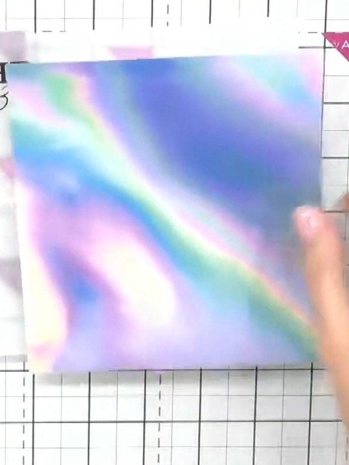 Step 5: Load a white ink pad and gently dab it onto the raised areas of the embossed design on the holographic paper. 