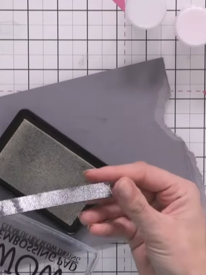 Step 2: Apply sticky ink to the first black strip using the ink pad. Sprinkle silver embossing powder over the inked s