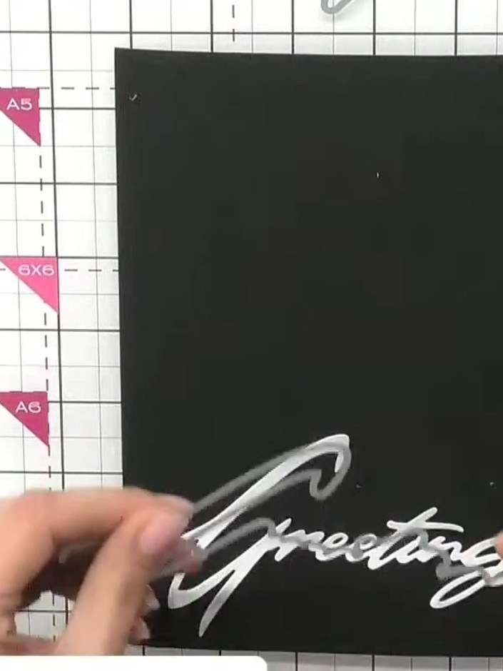 Step 5: Cut the word 'Greetings' from black card using the Christmas Snow Drift die. Position the die-cut word at an a
