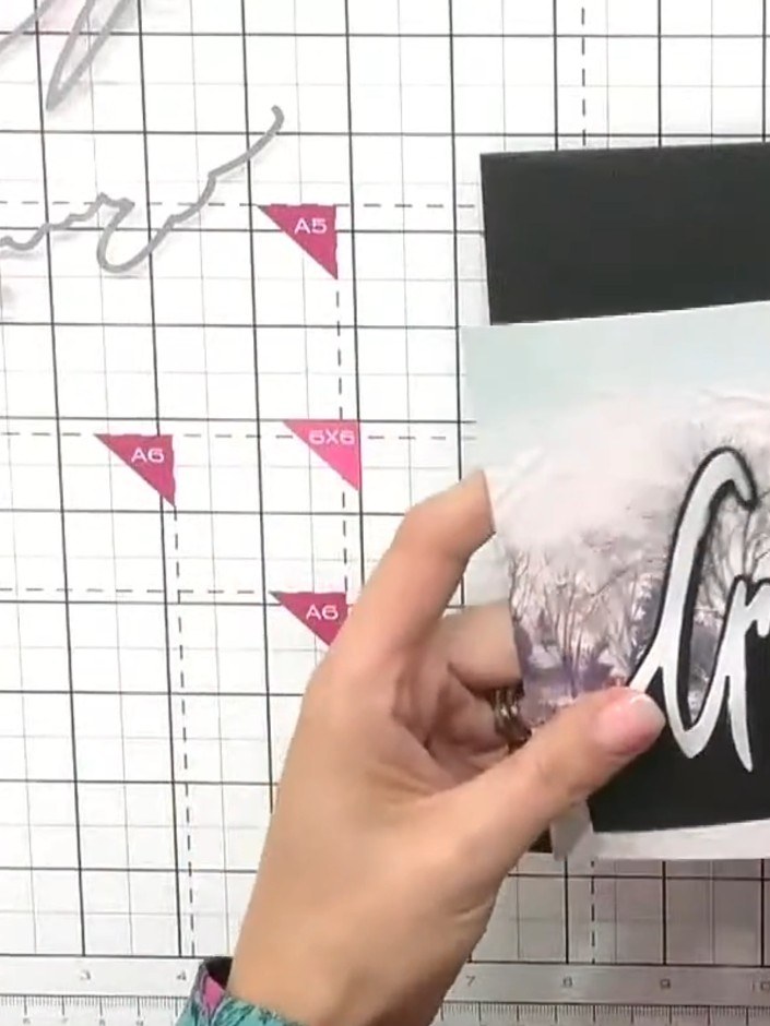 Step 7: Apply glue to the back of the mounted scene piece. Position it on the black card base so the 'Greetings' snow 