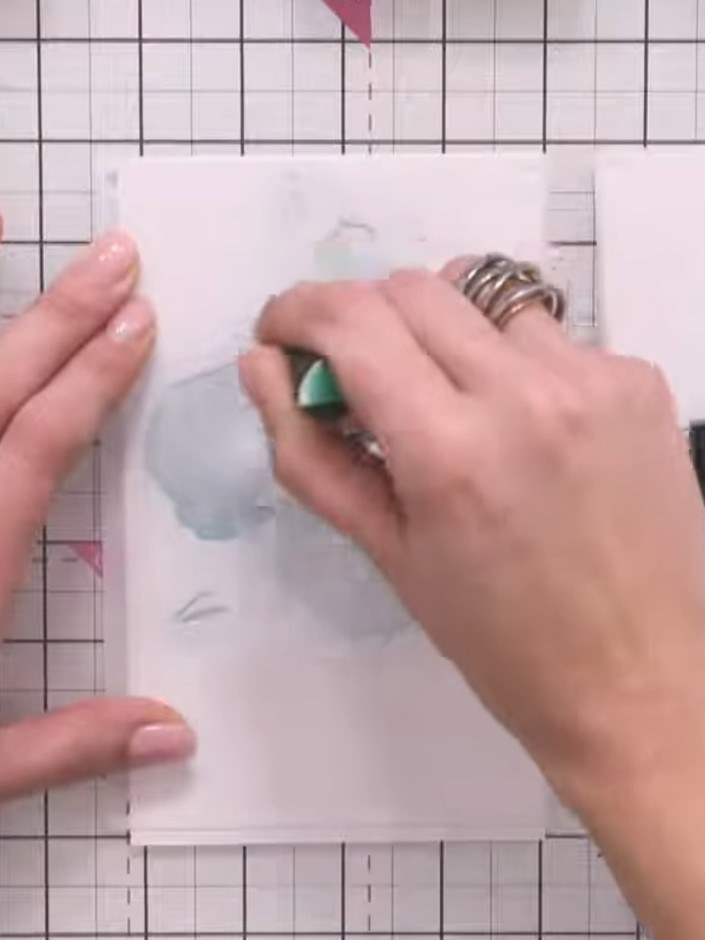 Step 2: Apply teal-coloured ink through the first stencil using an ink blending brush. Hold the stencil in place with 