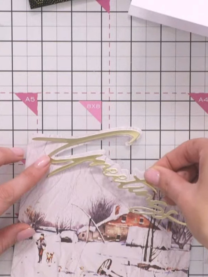 Step 6: Adhere the cut gold Greetings sentiment onto your card using glue, positioning it over the painted mount at th