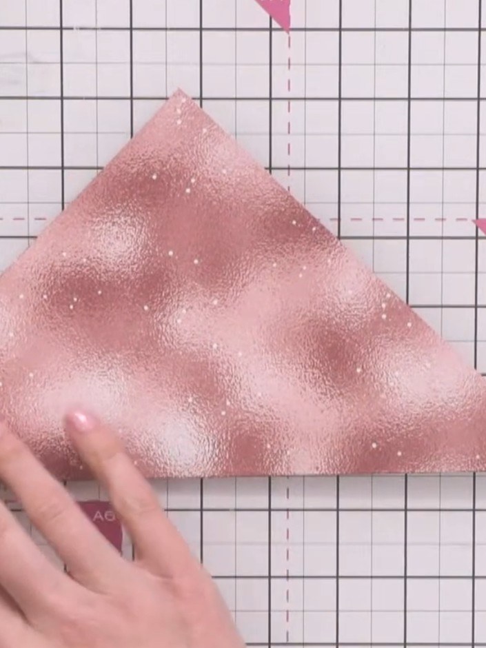 Step 2: Fold the bottom left corner of the pink glitter paper up to align with the top point, creating a triangle. Pre