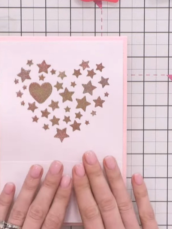 Step 11: Adhere the white panel down the centre of the pink card base. Layer the vellum heart with stars on top, follow