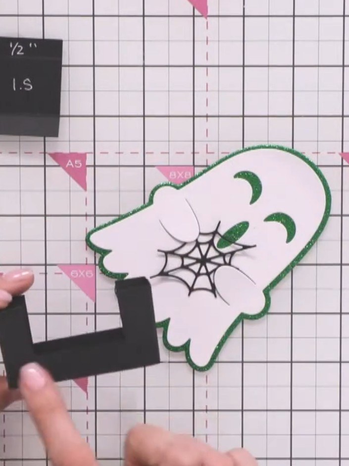 Step 10: Apply adhesive to the back of the second ghost character piece (with green glitter outline and spider web deta