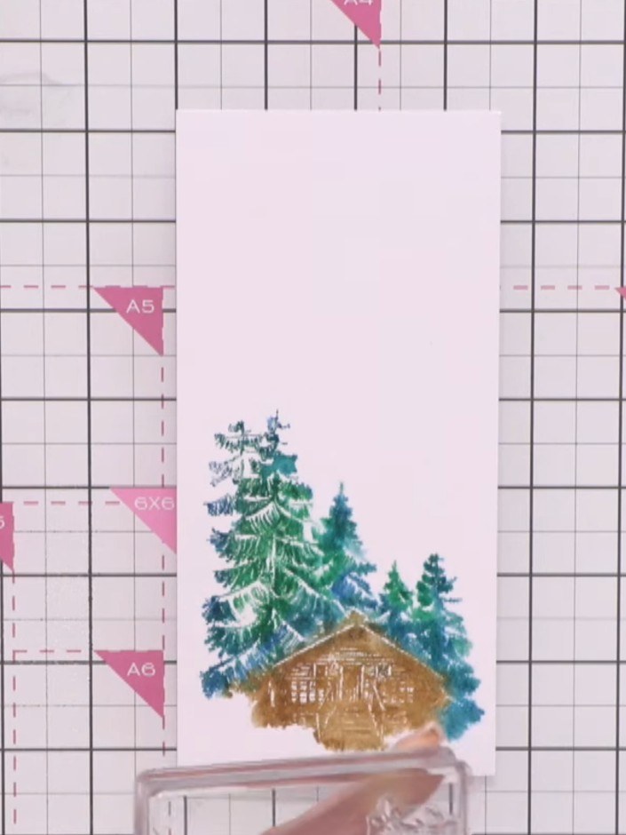 Step 4: Stamp the inked cabin image directly onto the wet watercoloured card near the base, allowing the ink to bleed 
