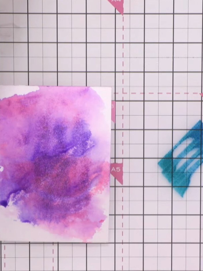 Step 6: Flick your fingers through one of the ink colours to create spatter texture across the watercoloured card back