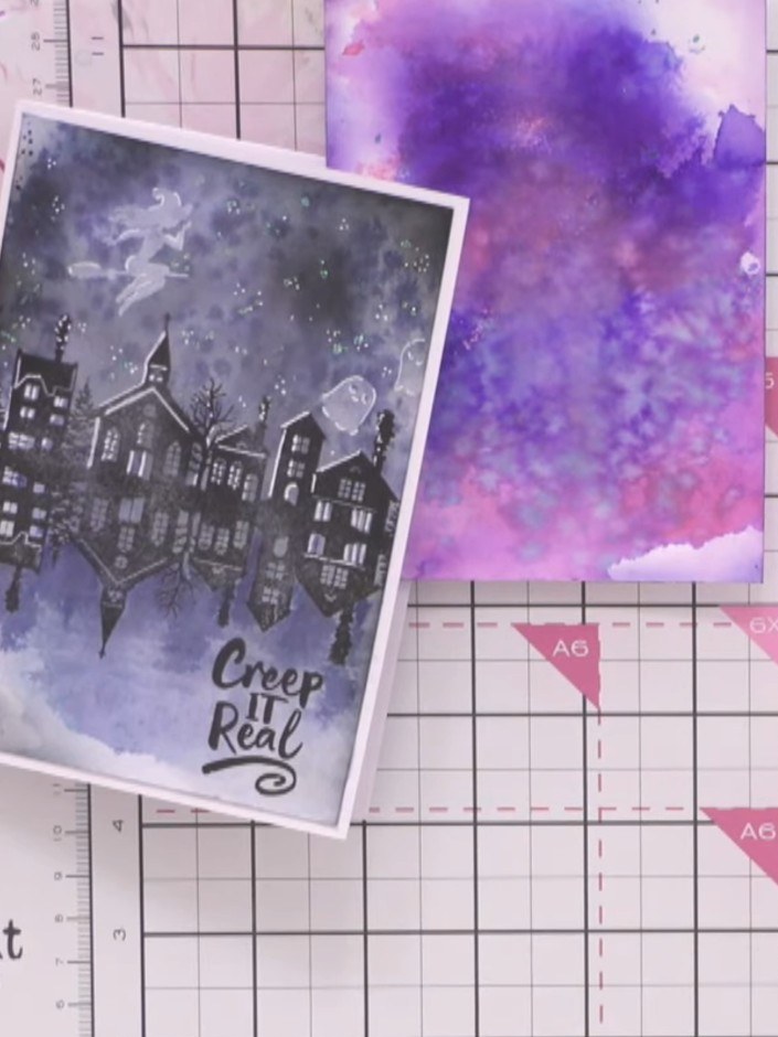 Step 11: Stamp the 'Creep It Real' sentiment in black ink at the base of the card, positioning it below the reflected b