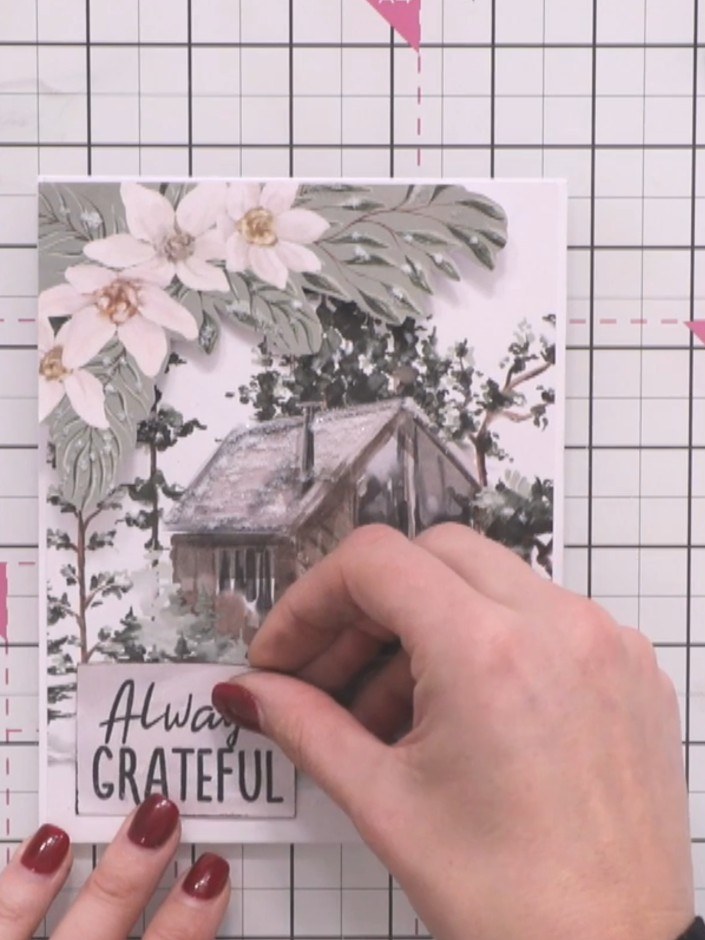 Step 12: Position the matted and padded sentiment reading 'Always GRATEFUL' on your card below the cabin scene, ensurin