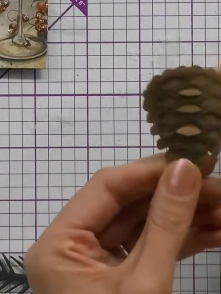 Step 10: Attach filler flowers and greenery around the pine cone to create a complete festive arrangement. Position the