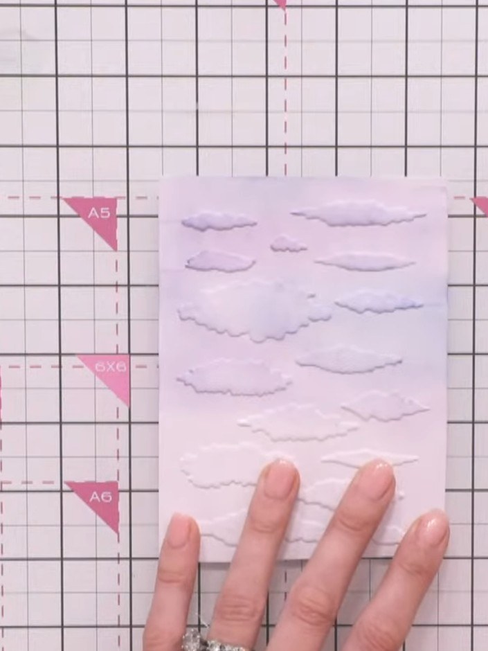 Step 7: Position the coordinating cloud stencil over your embossed and inked background, aligning it with the embossed