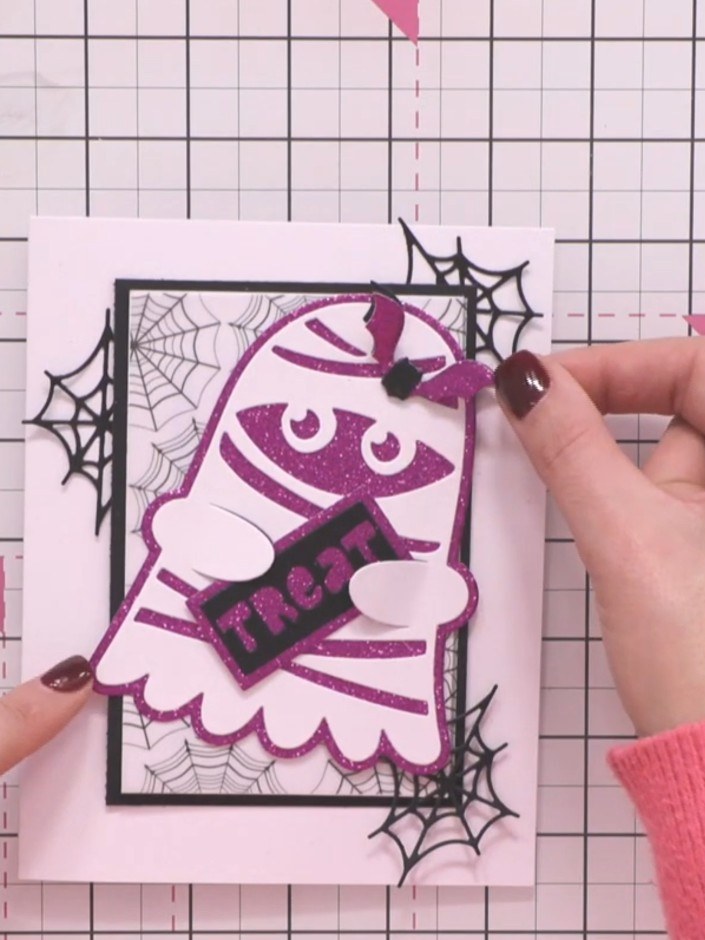 Step 10: Position the purple glitter bat hair clip on top of the ghost's head to complete the character card. The bat a