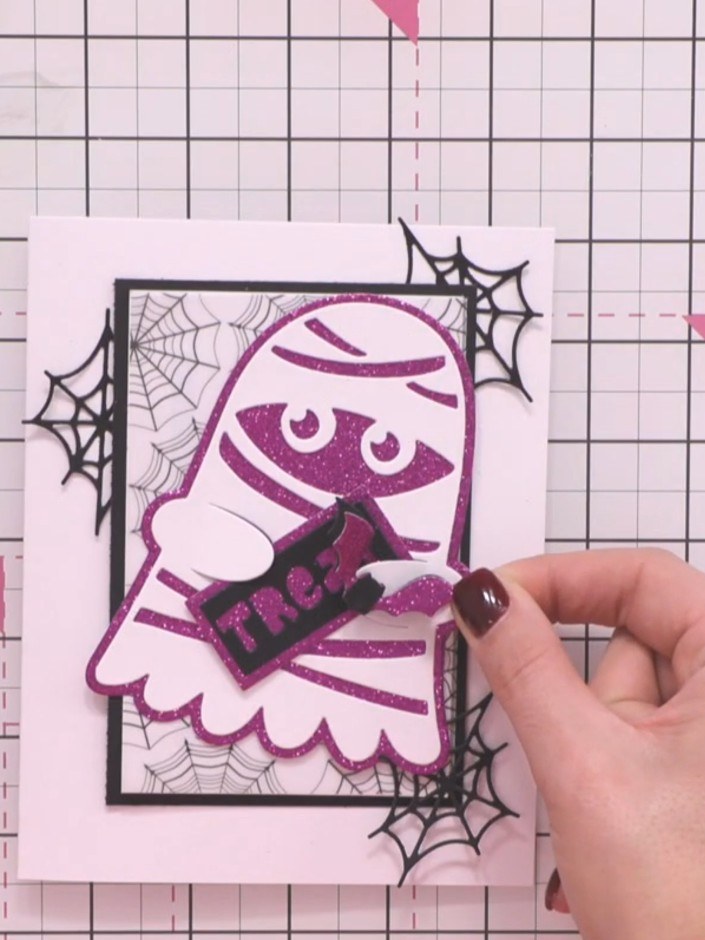 Step 9: Cut several bat die-cut pieces from purple glitter card. Arrange them on the ghost's head to create a decorati