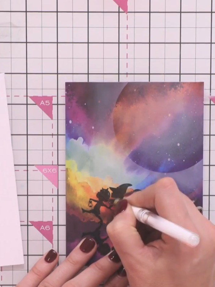 Step 8: Mount the decorated panel with the galaxy background and silhouette figures onto a white card base. Use adhesi