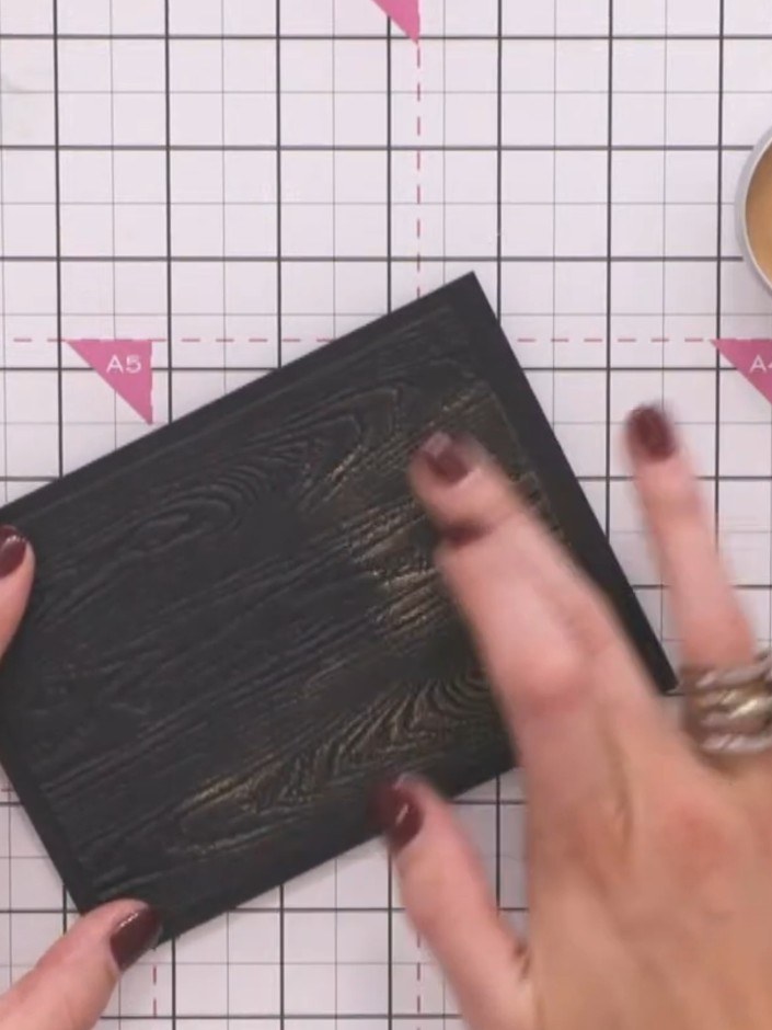 Step 4: Lightly swipe the gilding wax across the raised embossed details on the black card to highlight the wood grain