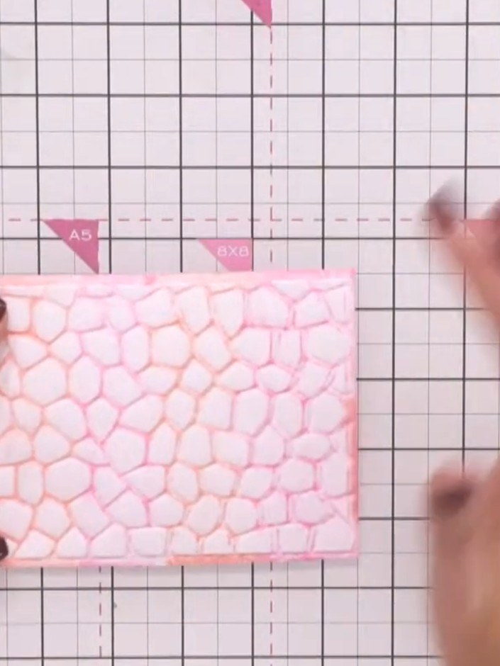 Step 8: Apply gilding wax to the raised embossed areas of the pink patterned paper using your finger, gently rubbing t