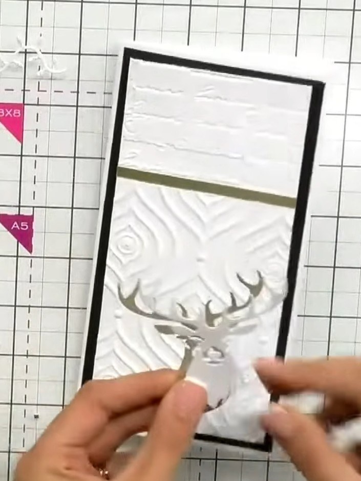 Step 4: Adhere the black-backed stag die-cut onto a gold decorative strip. Position this centrally on your white embos