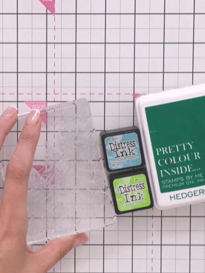 Step 2: Using an acrylic block, dab multiple shades of green Distress Ink onto the cabin stamp. Vary the tones across 