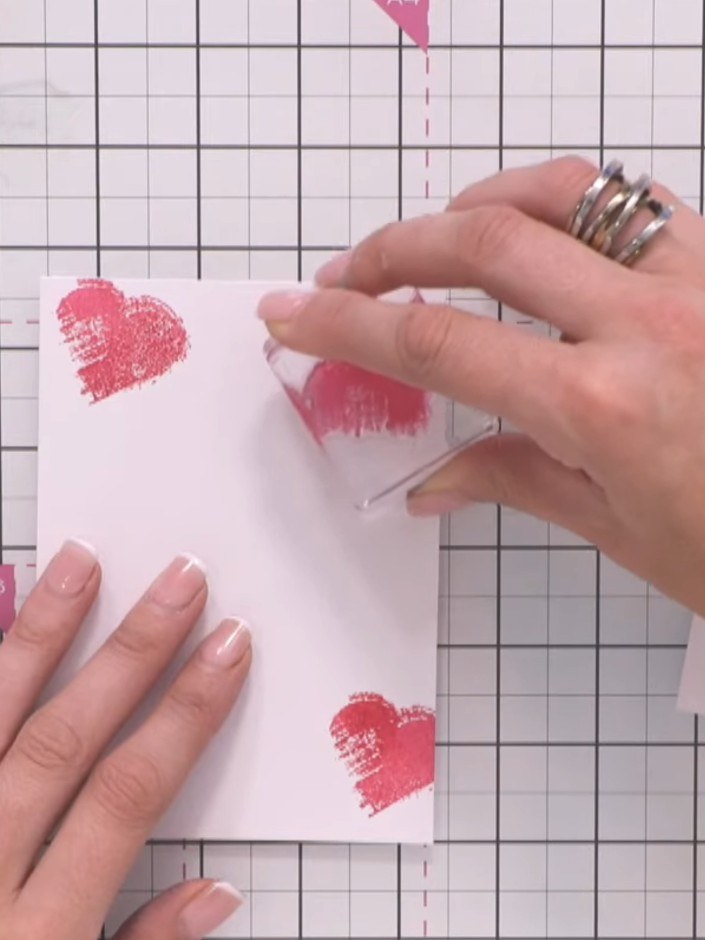 Step 2: Ink up the heart stamp in pink and stamp three hearts scattered across the card front. Position some hearts pa