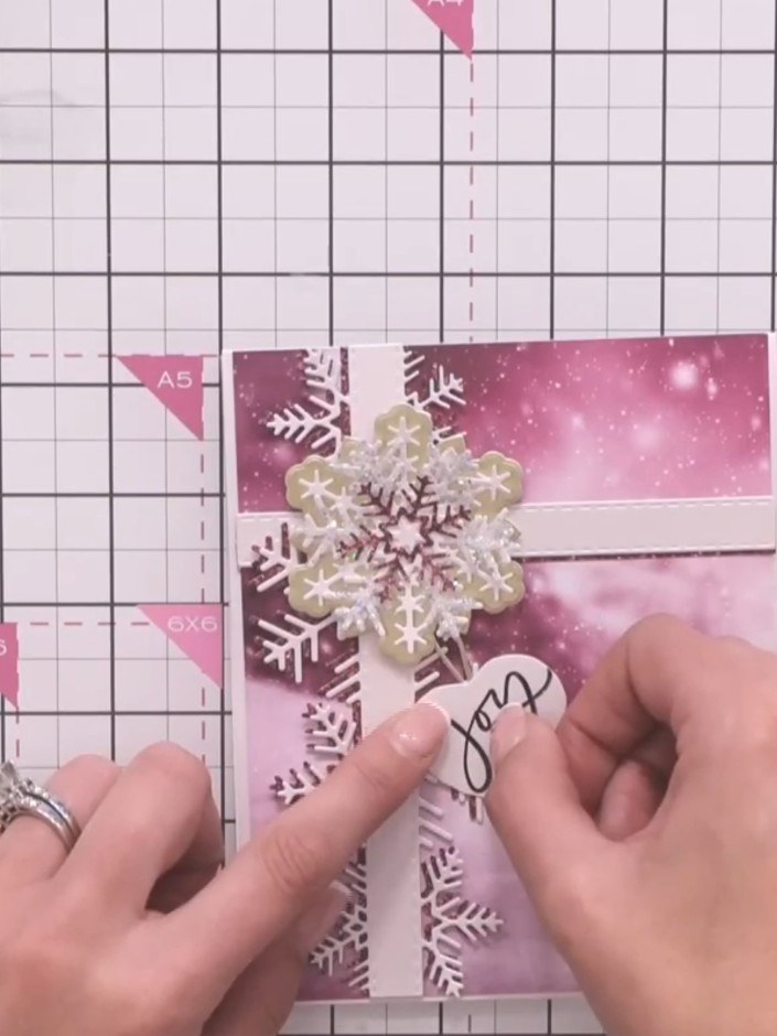 Step 8: Stamp the word 'Joy' onto a small tag die-cut using black ink. Position the stamp carefully on the pink tag be