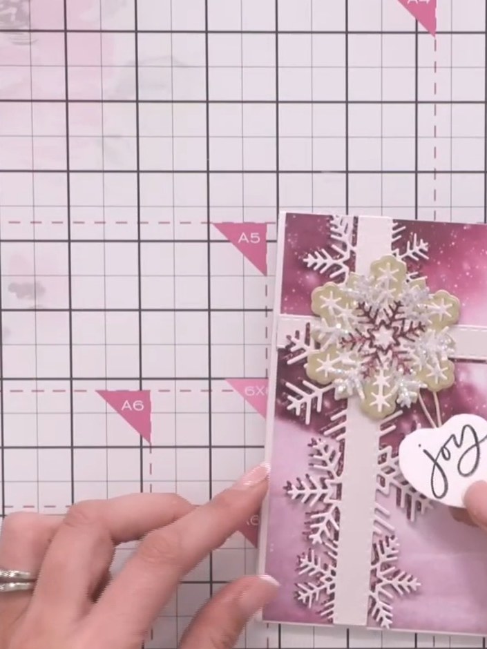 Step 9: Mete la etiqueta estampada con 'joy' detrás de la tira de borde de copos de nieve para que se asome por la parte de abajo de la tarjeta.