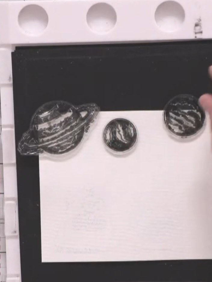 Step 7: Position planet stamps around the top of the white card panel. Stamp each planet, apply white embossing powder