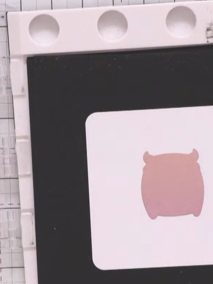Step 5: Position the pink monster-shaped mask over the stamped sentiment on the white square panel. Hold it in place w
