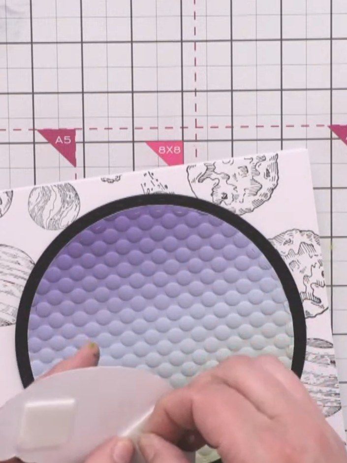 Step 11: Position and glue the large purple monster character at the bottom of the embossed circle. Add the smaller pin