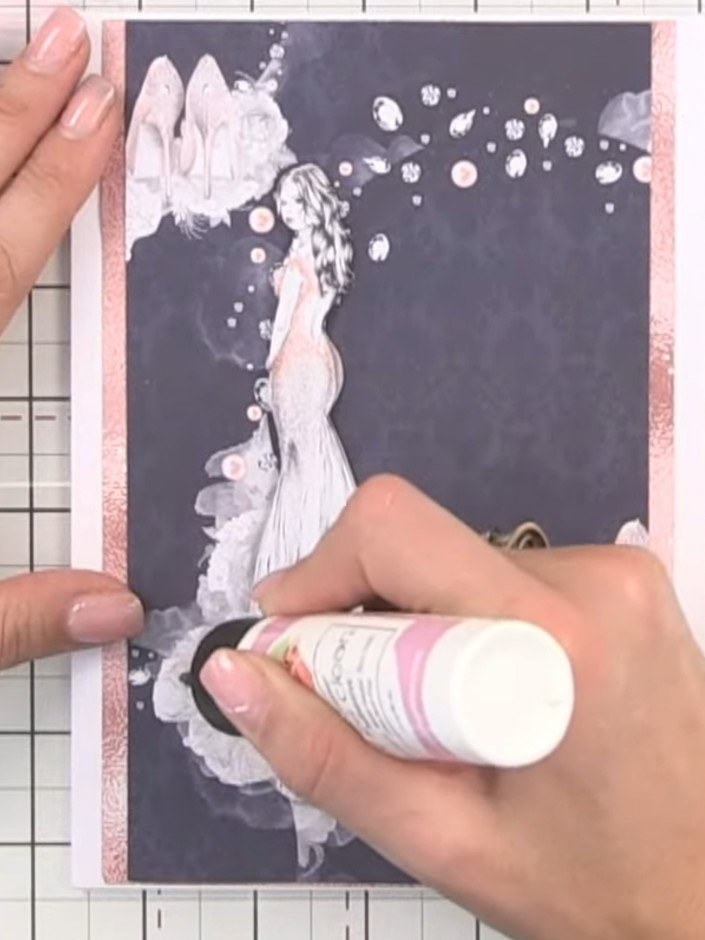 Step 5: Apply crystal clear glitter to the bottom of the dress on the card panel for sparkle. Hold a piece of pink car