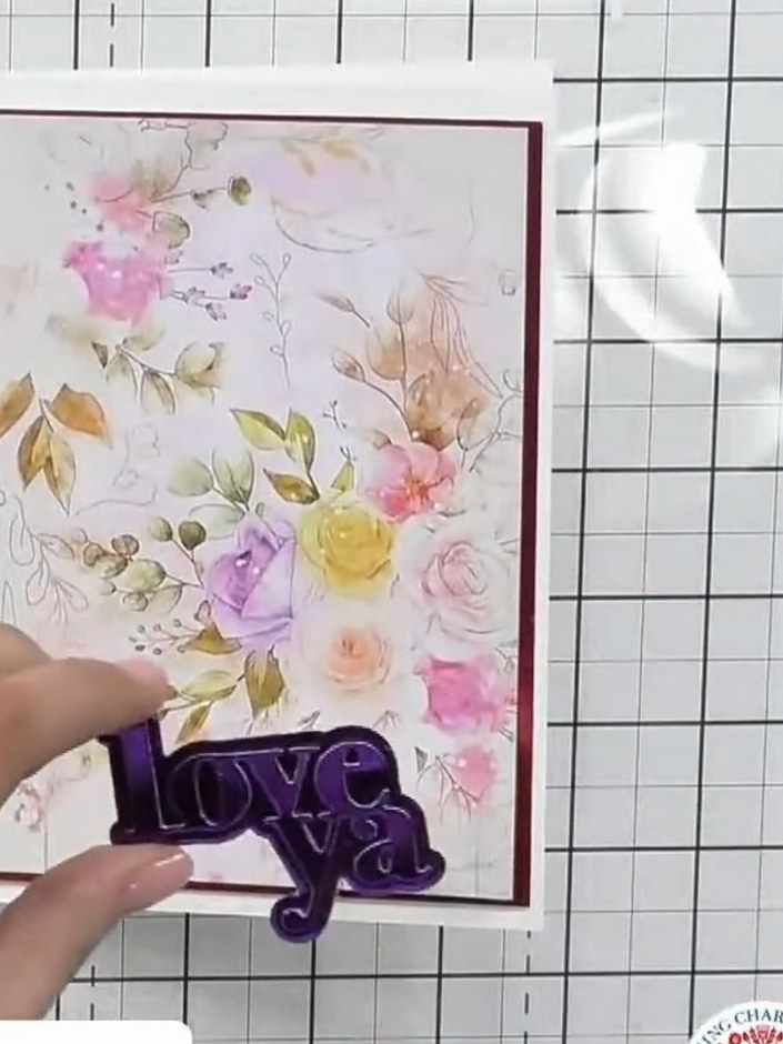 Step 5: Position the purple metallic 'love' sentiment on the card front near the bottom edge. Offset the white 'love' 